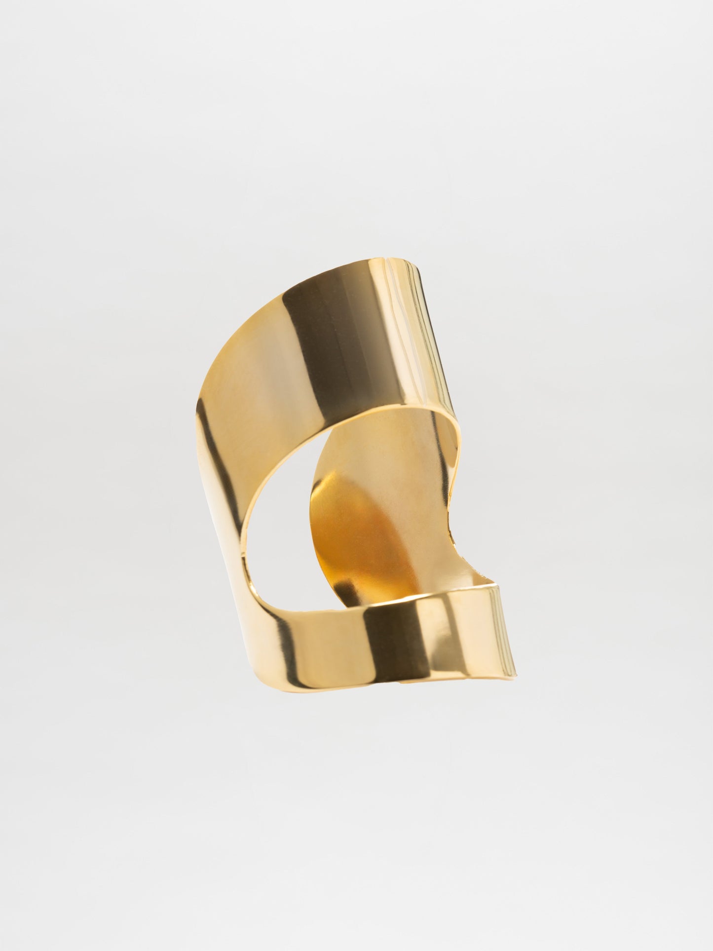 La escultura Cuff Artemis, con su acabado baño de oro, presenta superficies curvas y plegadas que brillan sobre un fondo blanco liso. Esta exquisita pieza cuenta con una textura suave que recuerda a un brazalete moderno y refleja la creatividad contemporánea en su diseño fluido.
