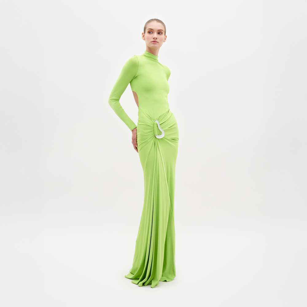 Sobre un fondo blanco, una persona lleva el Vestido Lena, un vestido largo verde claro con mangas largas. Confeccionado en tela italiana fina, tiene un diseño fruncido y adornos blancos en la cintura. Lleva el pelo recogido hacia atrás, lo que realza su expresión neutra.