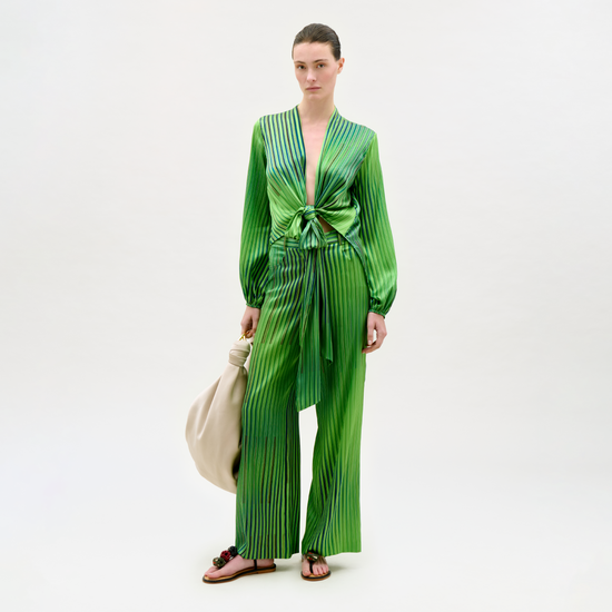 Woman wearing a green pleated outfit holding a beige handbag on a white background