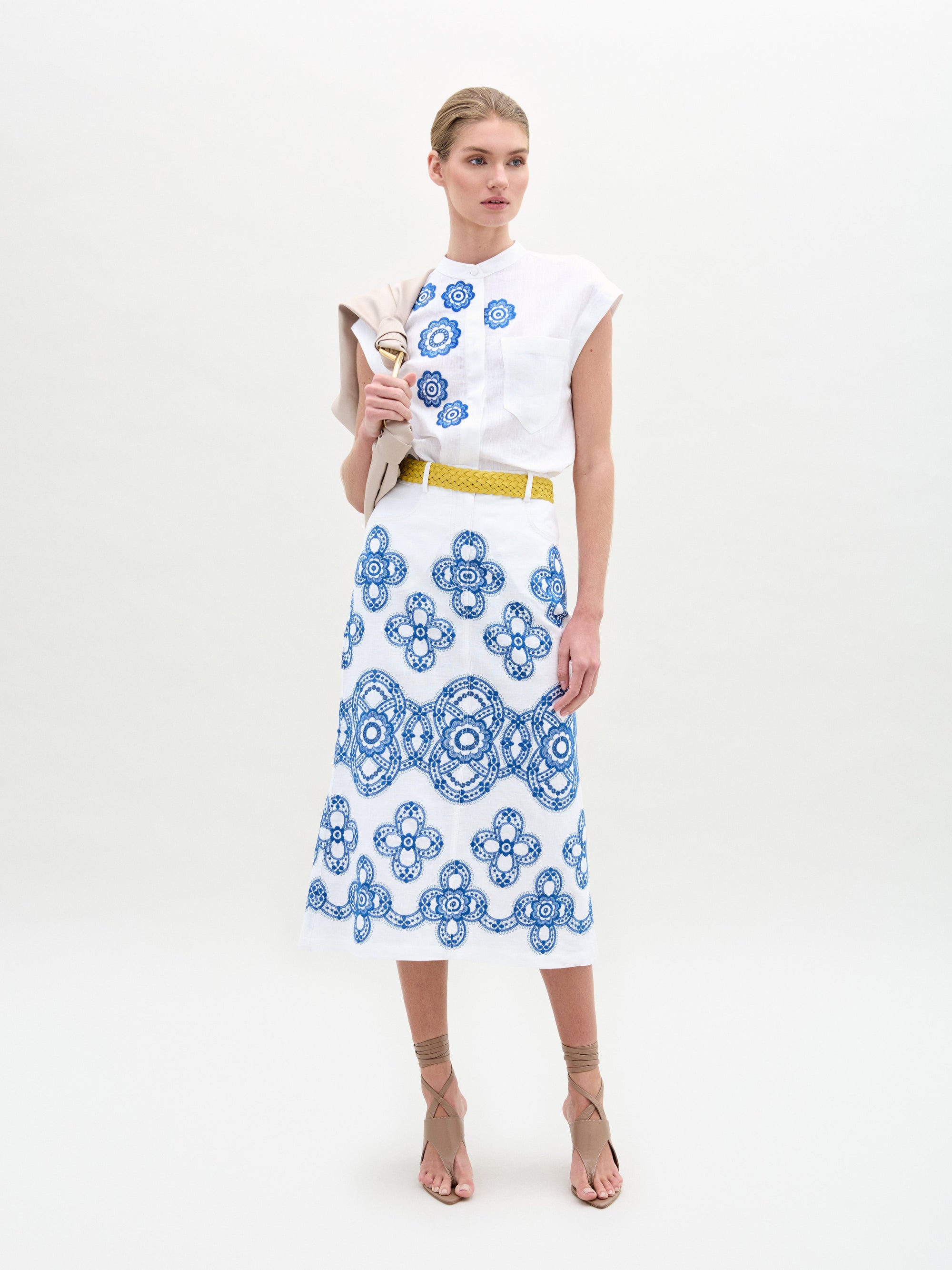 A person wearing a white top with the Layan Skirt, holding a beige jacket.