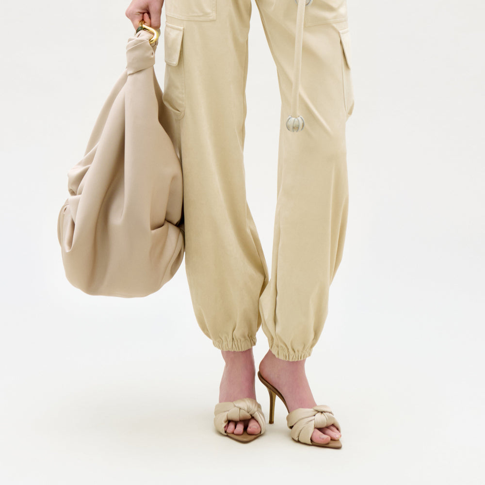 Person wearing beige pants and holding a matching handbag on a white background