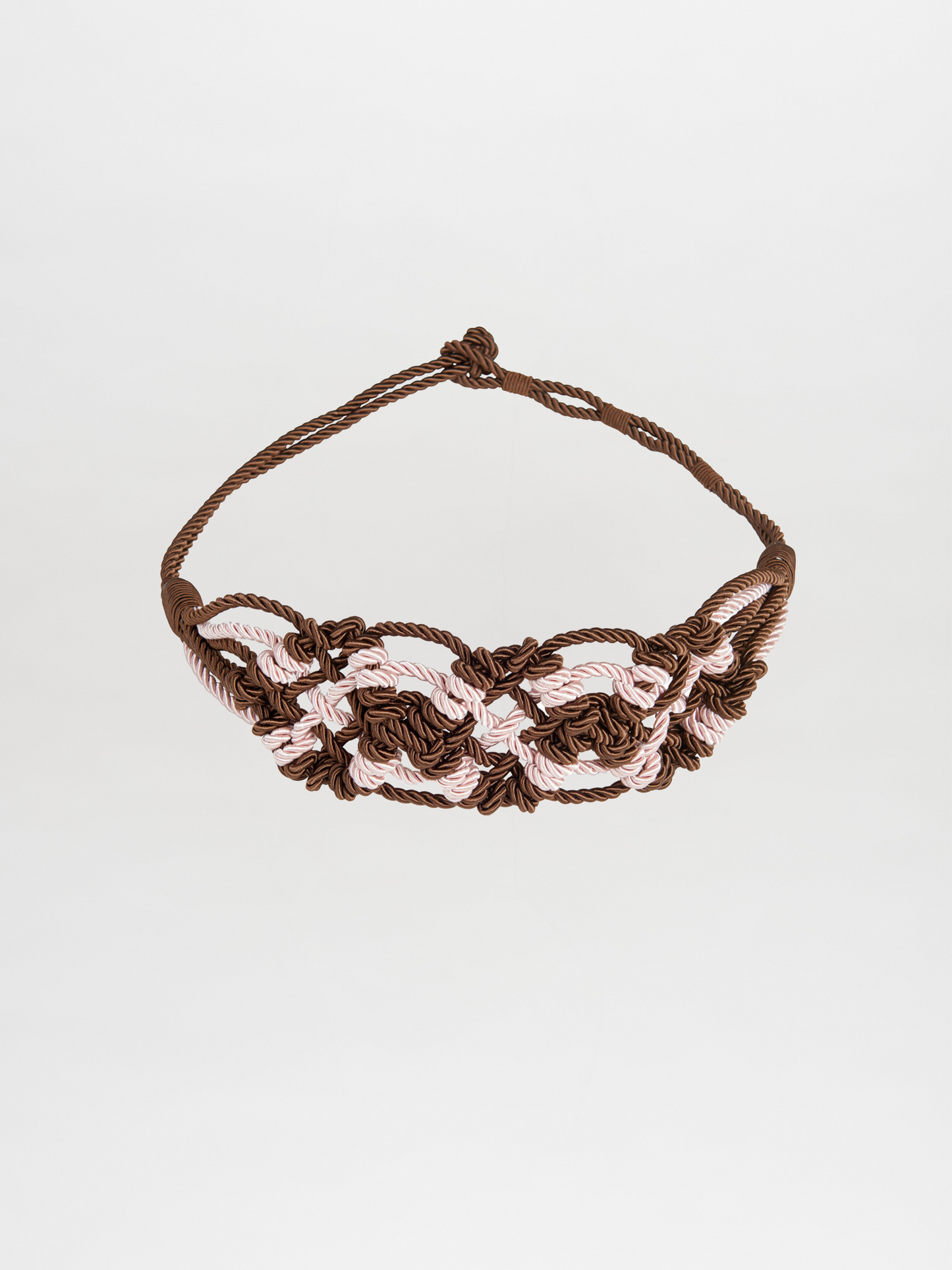 The Bresia Belt Brown Pink features intertwined brown and light pink cords that create a woven pattern reminiscent of nautical knots, set against a plain white background. This accessory adds a touch of elegance to any outfit and is ready to ship, arriving just days after ordering.
