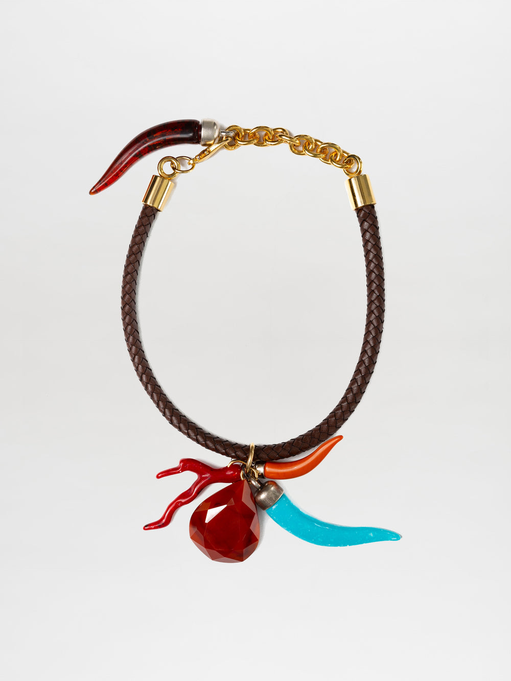 El collar Leslie presenta una banda marrón trenzada con detalles metálicos, un cierre de cadena dorada y tres dijes: una joya roja, un cuerno rojo y un cuerno azul. Los adornos multicolores están unidos cerca del cierre con anillos dorados.