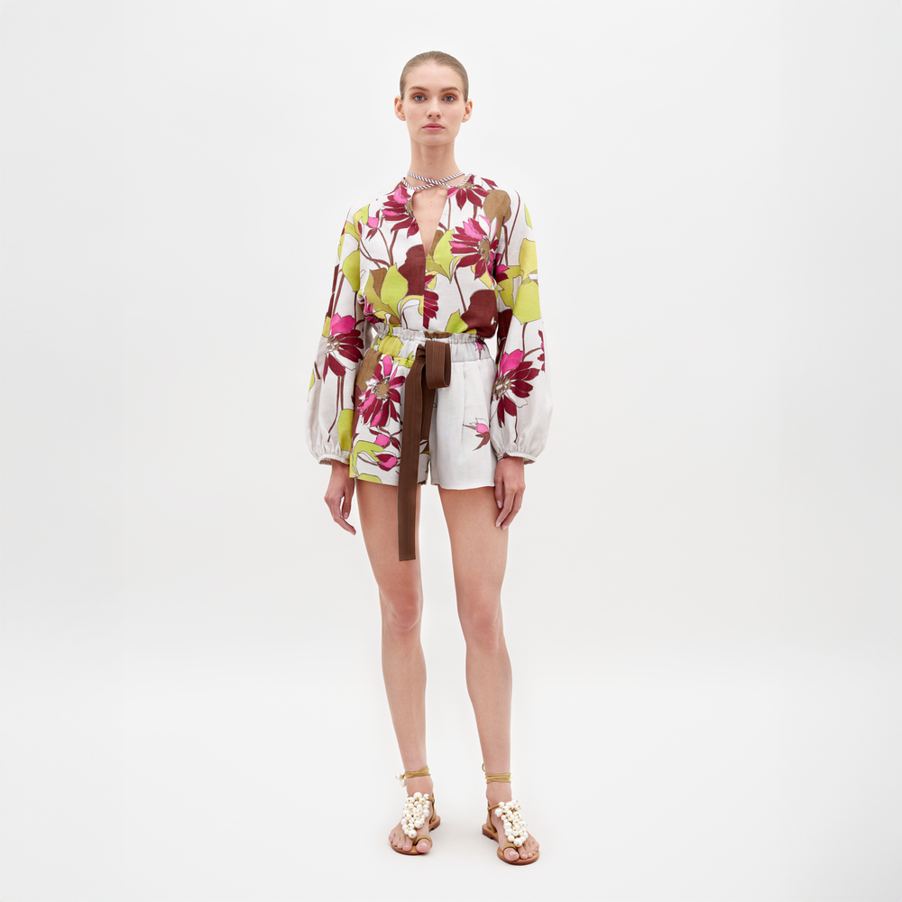 Con el short Giorgio, una persona luce una blusa floral con diseños verdes y morados sobre un fondo blanco liso. Combinada con shorts blancos de cintura alta de lino 100 %, el atuendo se complementa con un cinturón marrón, sandalias adornadas y una gargantilla.