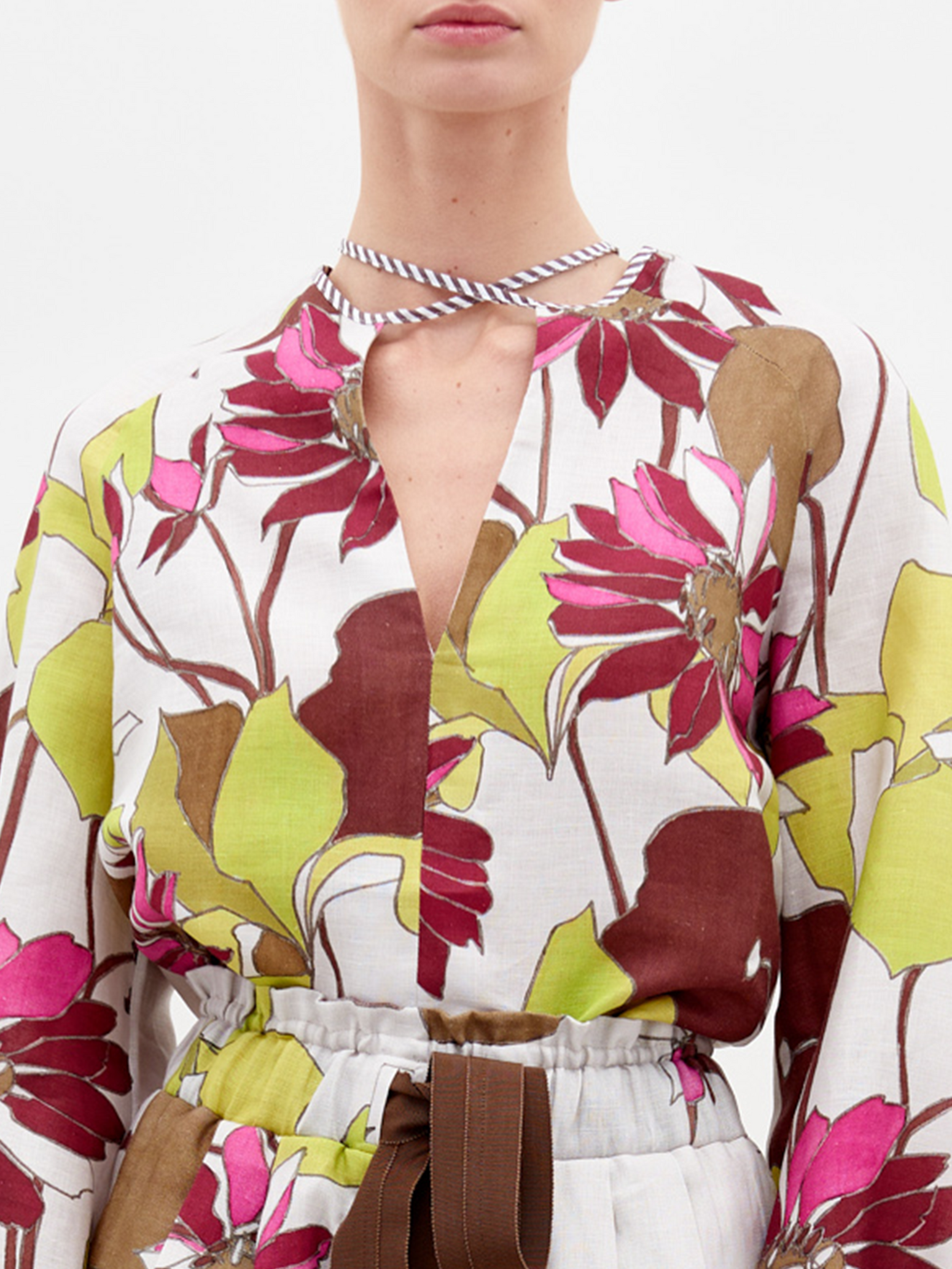 La Blusa Molveno es un conjunto de manga larga confeccionado en Colombia que presenta un estampado floral con flores grandes rosas y marrones y hojas verdes. Confeccionada en lino 100 % blanco, incluye un escote en V con una corbata de rayas. Combínala elegantemente con faldas o pantalones fruncidos a la cintura.