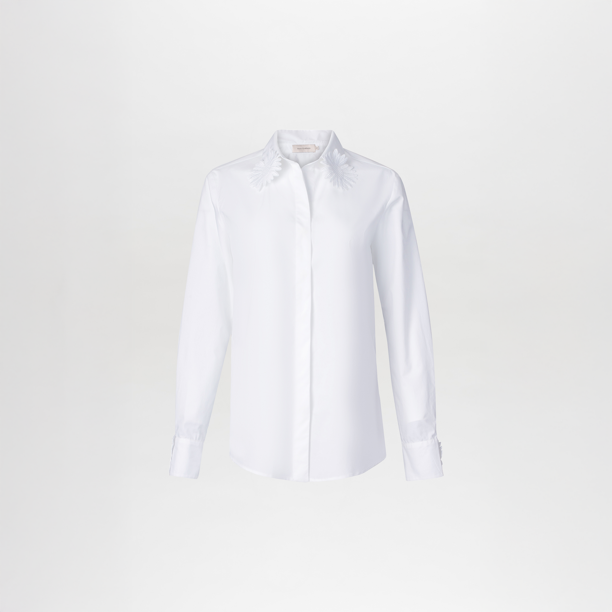 Person dressed in the Naroa Blouse White with a floral shirt and gold belt, standing against a blue background, ready to celebrate September 2nd.